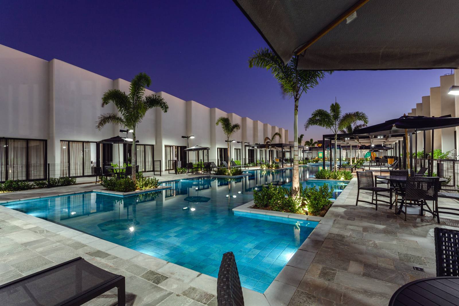 Piscina iluminada à noite, com os lofts e as palmeiras