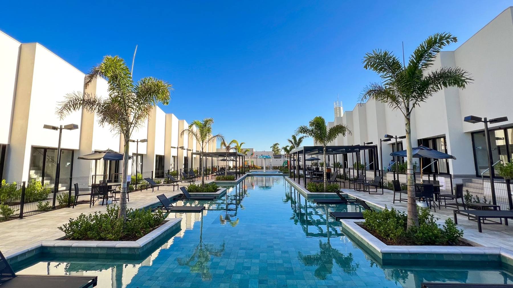 Piscina longa entre as duas fileiras de lofts, com palmeiras e espreguiçadeiras dentro d'água