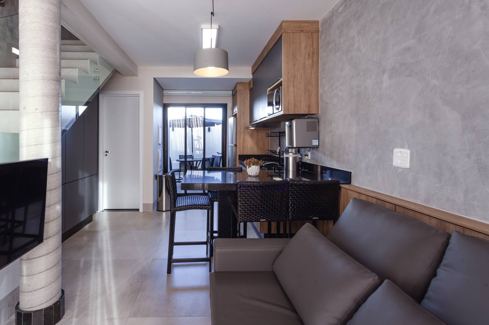 Sala com sofá, cozinha com bancada alta e, ao fundo, a porta de vidro para a área externa