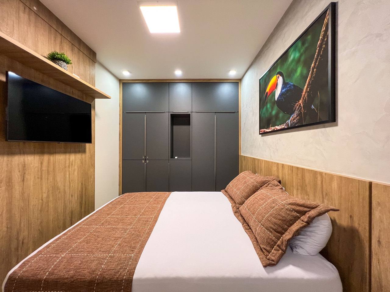Suíte com cama de casal, TV, armário planejado e quadro de tucano